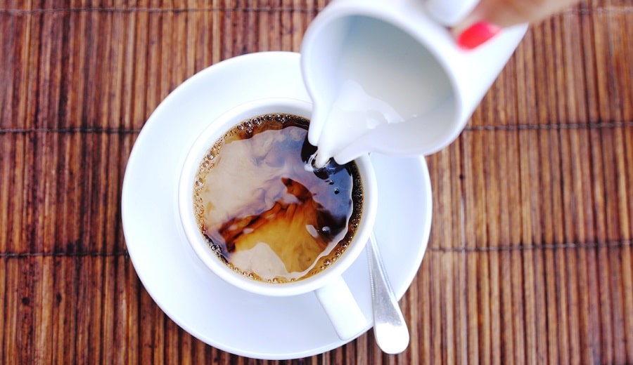 Top of view of pouring stream milk into a cup of espresso on a wooden table.